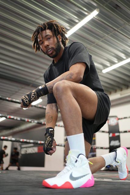 Een sporter met zwarte handwraps zit op één knie op het canvas in de zaal van Simson Gym en kijkt rustig in de camera