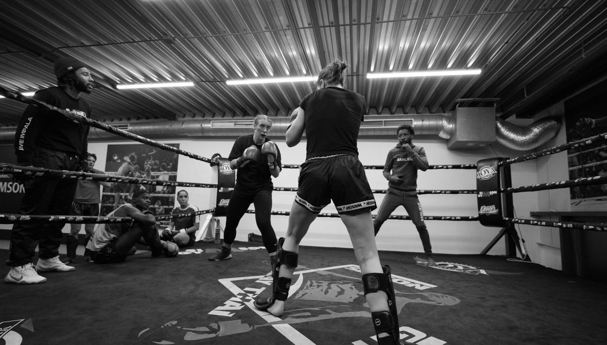 De trainingszaal van Simson Gym in zwart-wit, met de ring, trainers en sporters